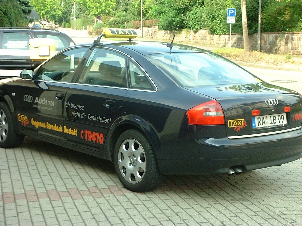 Dunkelblaues Taxi von Taxi-Holl mit gelbem Dachschild, der Aufschrift Gaggenau Gernsbach Rastatt, der Rufnummer 19410 und dem Spruch Ich bremse nicht für Tankstellen