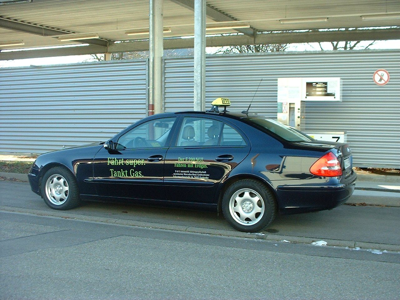 Dunkle Limousine mit Taxischild an einer Erdgas-Zapfsäule, auf der Tür die Aufschrift Fährt super. Tankt Gas.