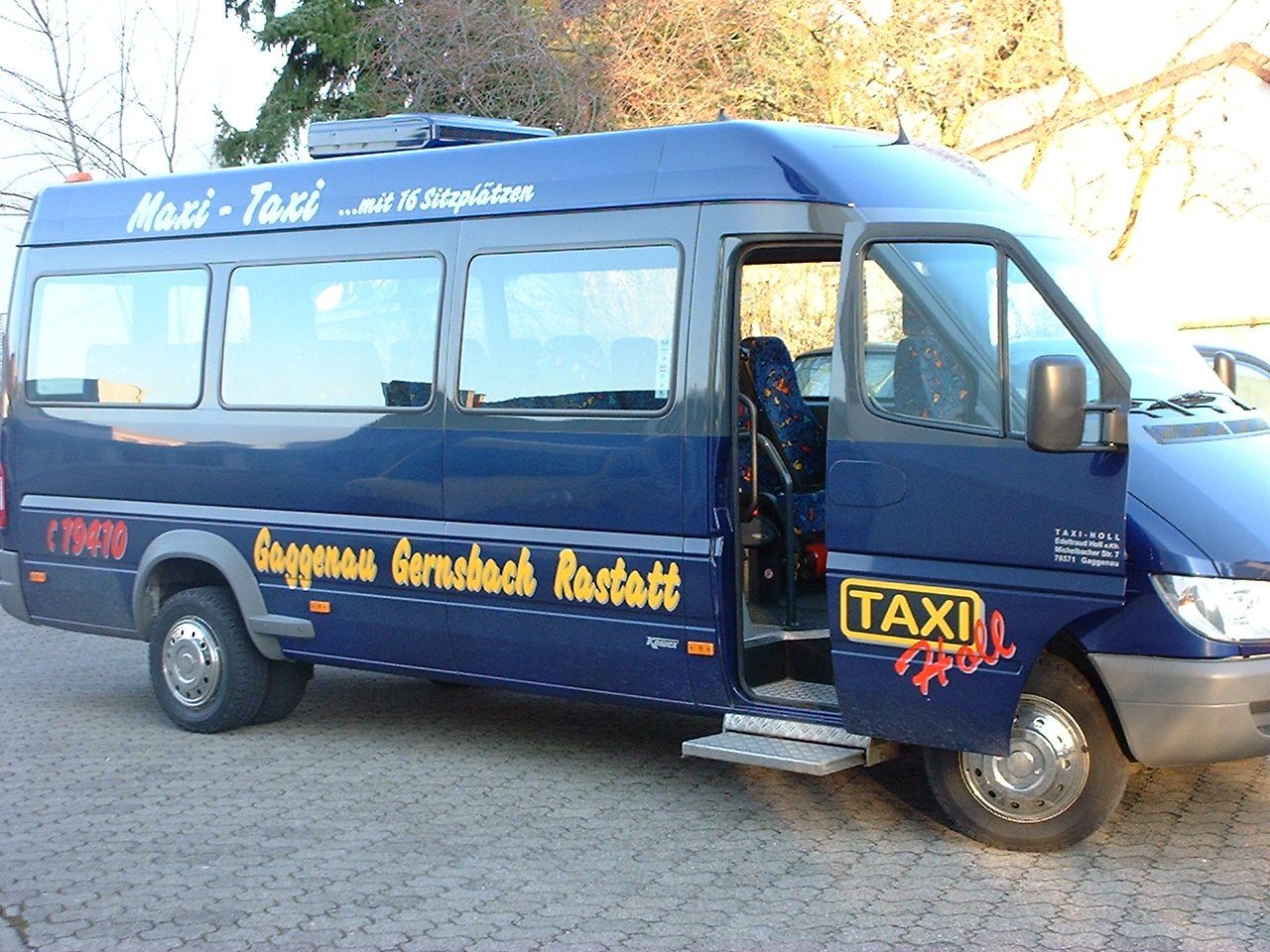 Dunkelblauer Kleinbus mit der Aufschrift Maxi-Taxi mit 16 Sitzplätzen, Gaggenau Gernsbach Rastatt und dem Taxi-Holl-Logo, Schiebetür und Fahrertür geöffnet