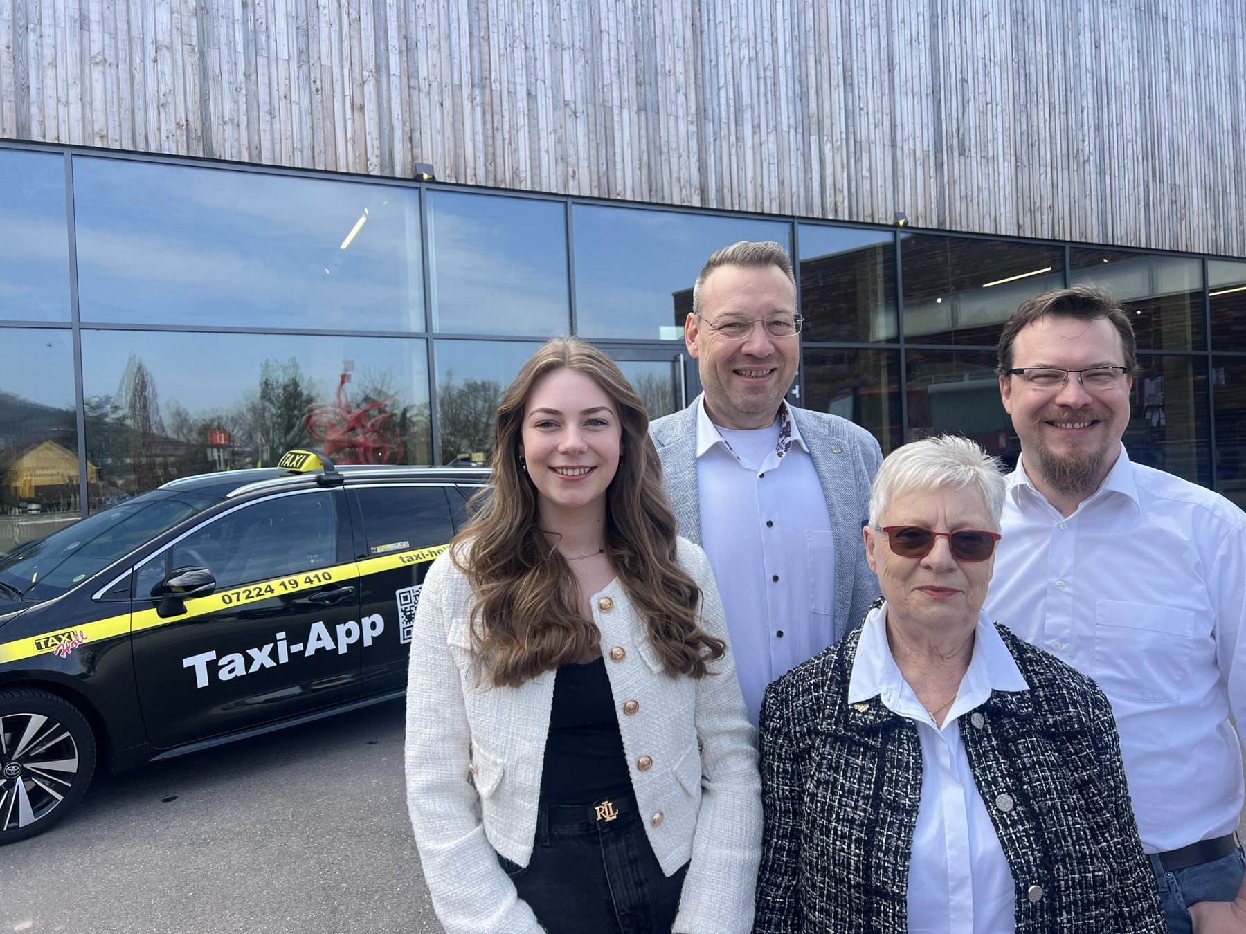 Romy, Dirk, Edeltraud und Sebastian Holl lächeln in die Kamera, im Hintergrund ein Taxi von Taxi-Holl
