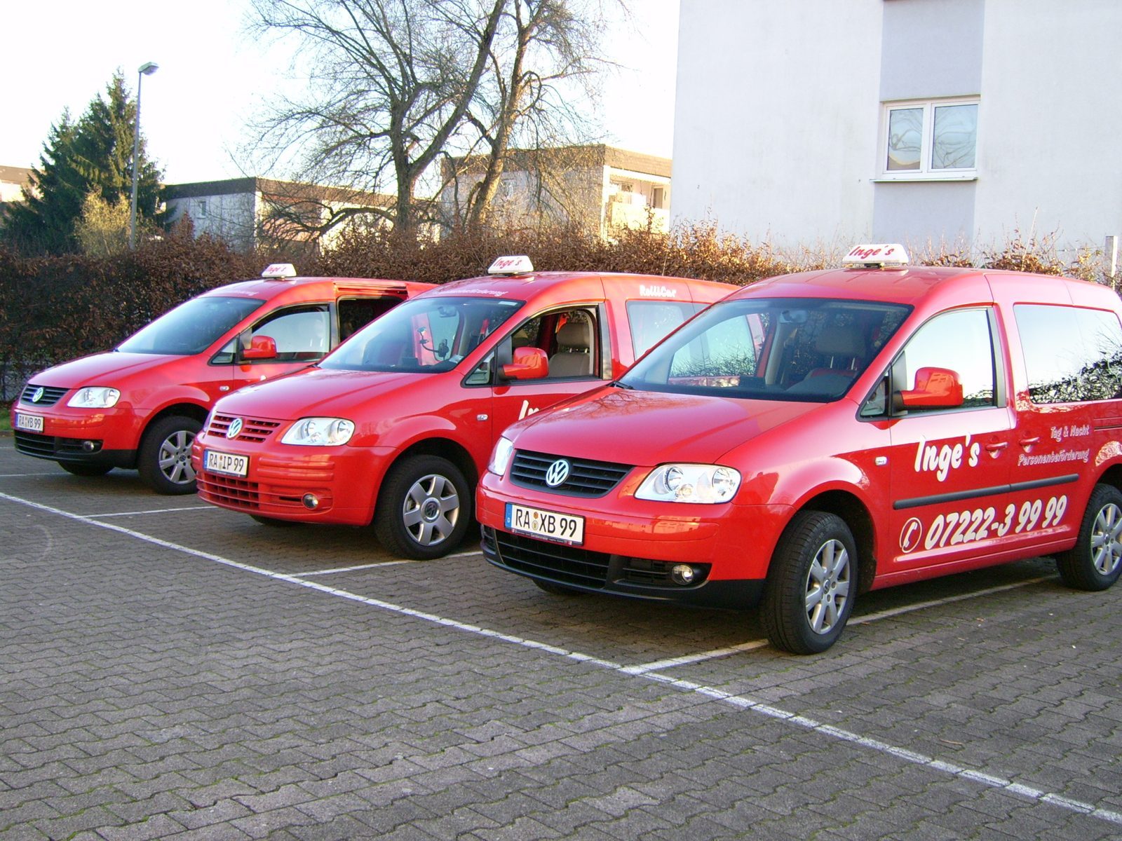 Drei rote Kleinbusse mit der Aufschrift Inge’s Personenbeförderung und der Rastatter Telefonnummer auf einem Parkplatz, einer davon als RolliCar beschriftet