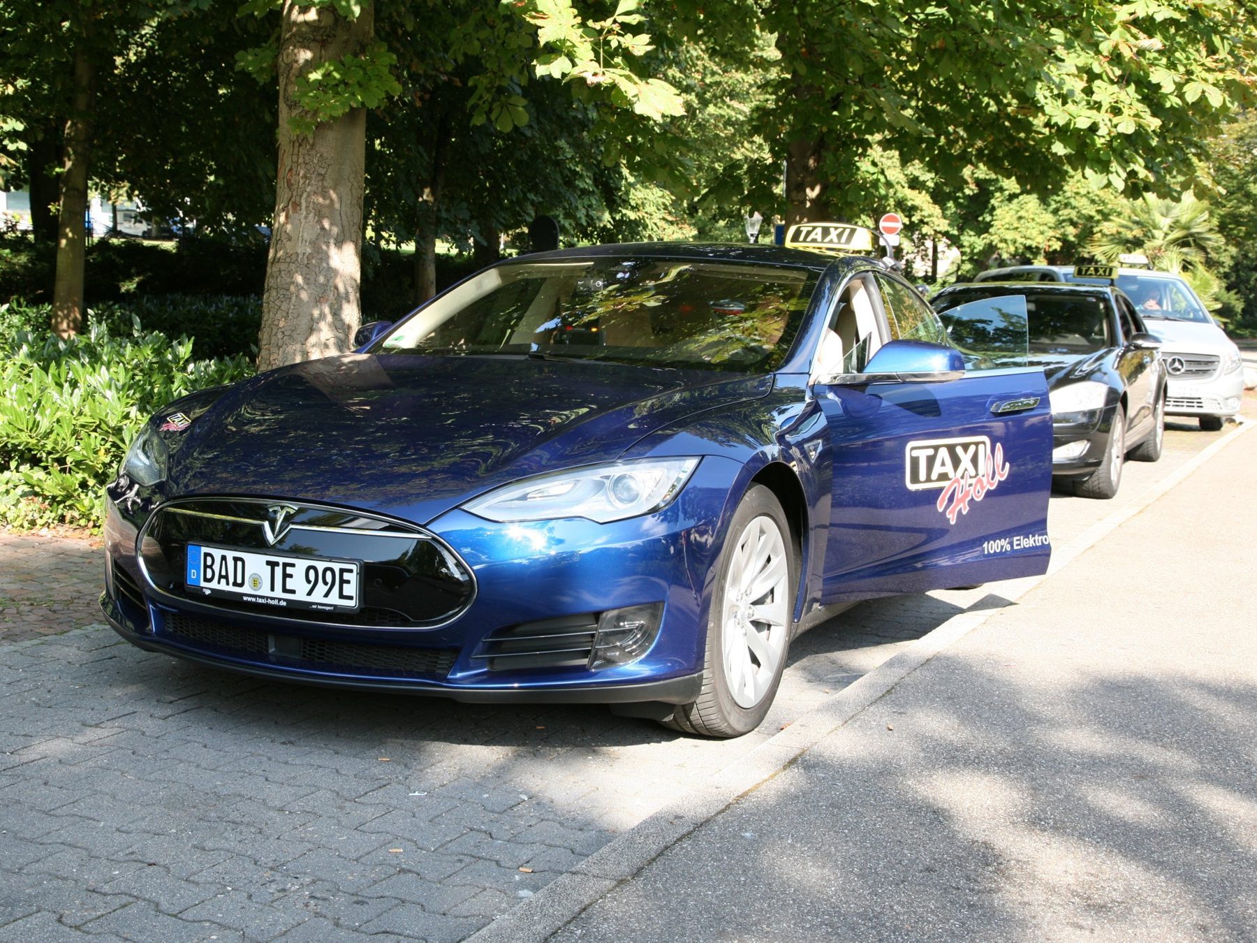 Dunkelblaues Elektrotaxi mit gelbem Dachschild und der Aufschrift 100 % Elektro
